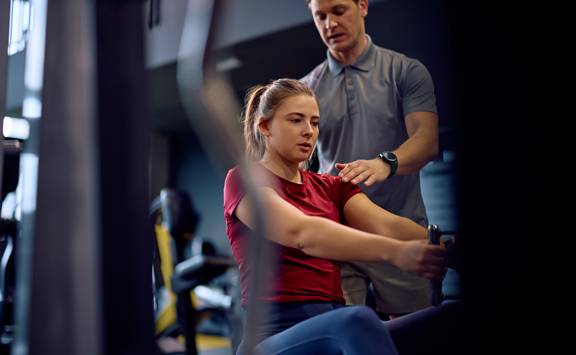 Athletic Woman Working Out Exercise Machine With Personal Coachs Assistance (1)